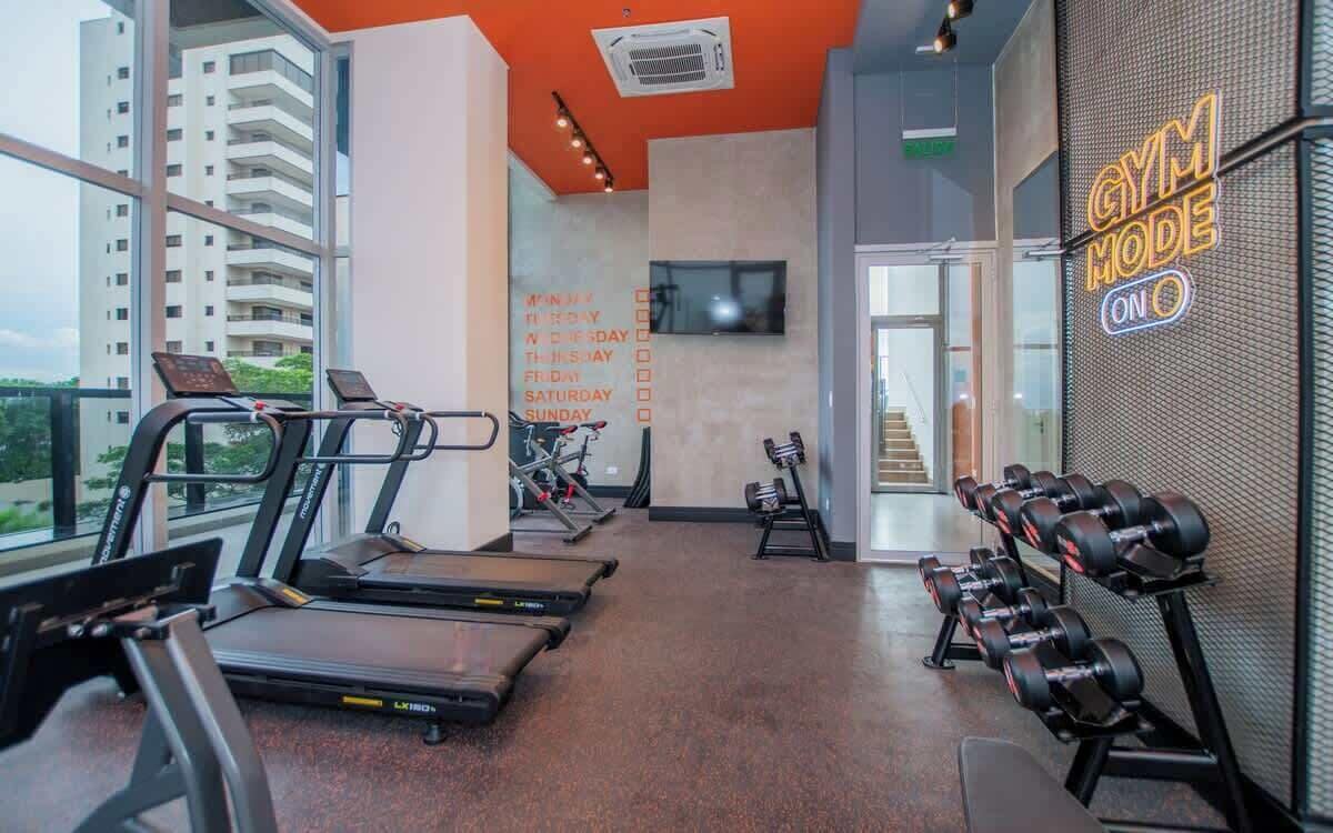 A gym with treadmills, dumbbells, and a wall with a schedule.