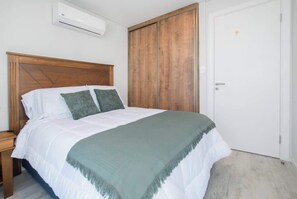 A bedroom with a wooden headboard, a bed with white bedding and a green throw, a wardrobe, and an air conditioning unit. - High-Floor City Base 200Mbps Gym, Pool & Sauna (Asunción)