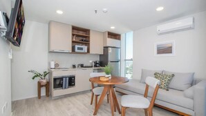 Een moderne keuken met inbouwapparatuur, een eethoek met een ronde tafel en stoelen, en een grijze bank met een kussen.