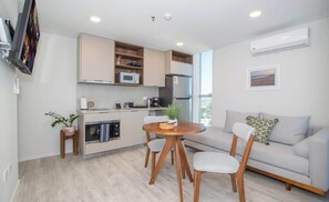 A modern kitchen with built-in appliances, a dining area with a round table and chairs, and a grey sofa with a cushion. - High-Floor City Base 200Mbps Gym, Pool & Sauna (Asunción)