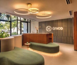 A modern reception area with a wooden desk, green seating, and a patterned wall. - High-Floor City Base 200Mbps Gym, Pool & Sauna (Asunción)