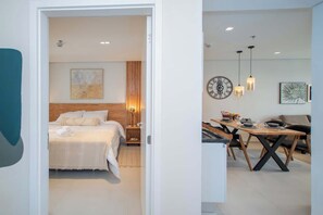 A modern hotel room with a bed, bedside table, and a dining area with a table and chairs. - Sleek 1BR Apt, City Views & Pool (Asunción)