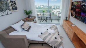 A modern bedroom with a bed, a sofa, a TV, and a balcony with a view. - Sleek 1BR Apt, City Views & Pool (Asunción)