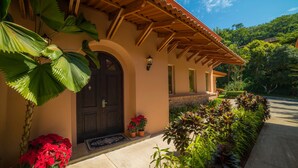 Un edificio con una pérgola de madera, una puerta oscura y un jardín bien cuidado con diversas plantas y flores.