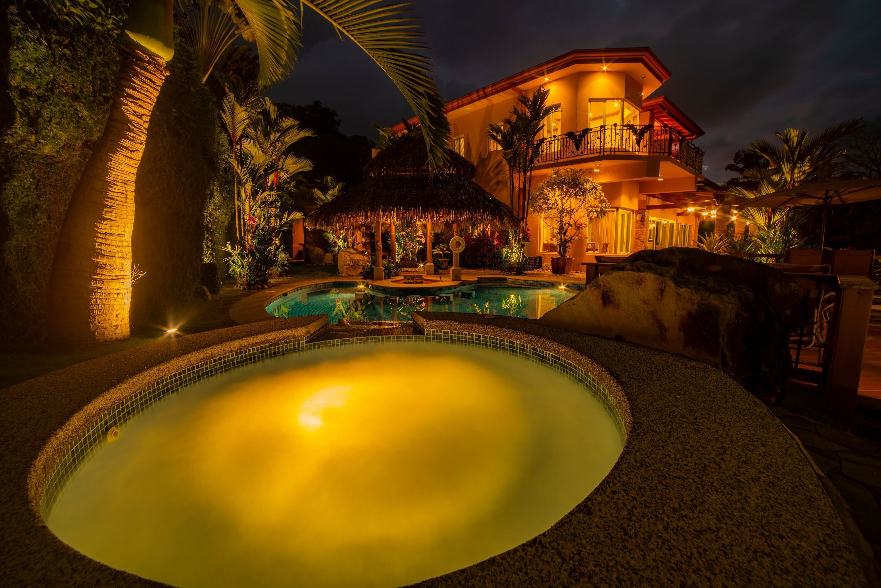 Um resort com piscina, uma construção de palha e um edifício bem iluminado.