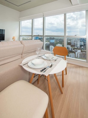 Une chambre moderne avec une table à manger pour deux personnes, un canapé et une vue sur la ville grâce à de grandes fenêtres.