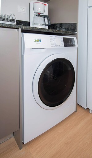 A compact, modern kitchen with a Bosch coffee maker, a white washing machine, and a granite countertop. - Urban 1-Bedroom Escape in Petra Tower Asuncion (Asunción)