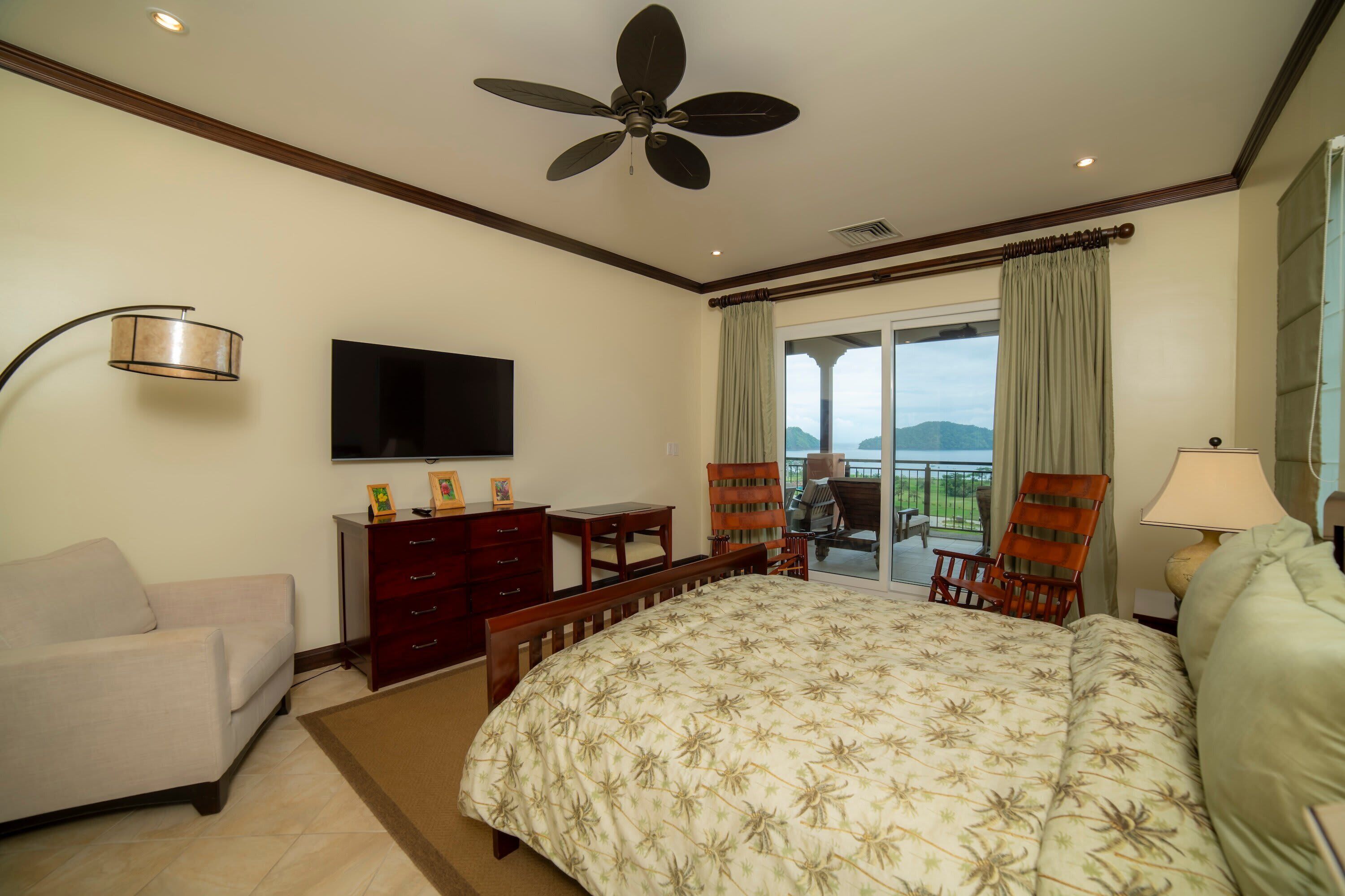 Habitación de hotel con cama, escritorio, silla, televisor y balcón con vistas.