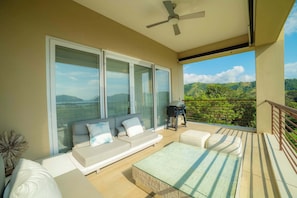 Un balcon avec un canapé, une table en verre et une vue sur la verdure et les collines.