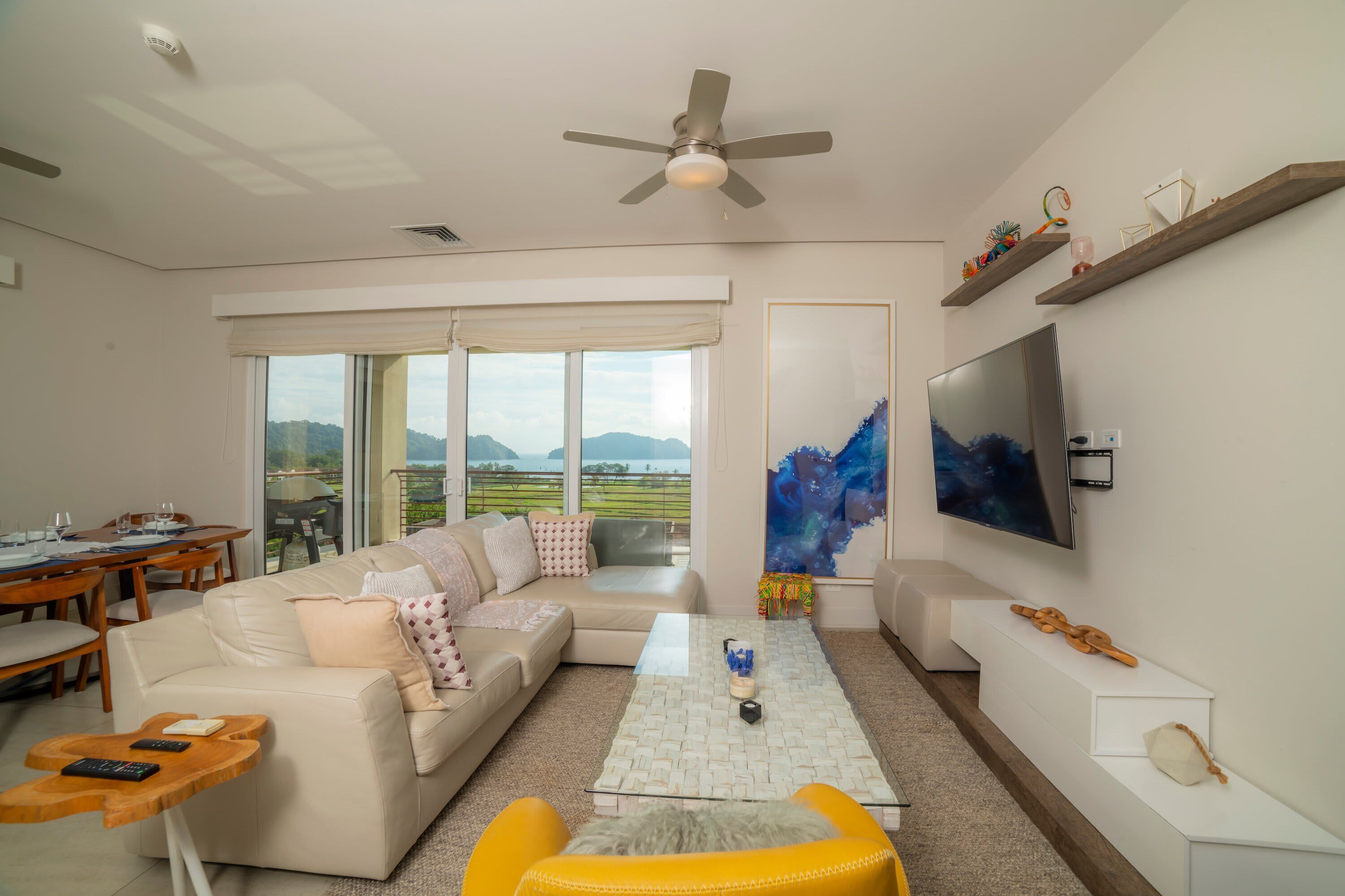 Un salon moderne avec un canapé, une table basse, un téléviseur et un balcon offrant une vue agréable.