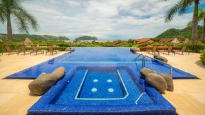 Una grande piscina esterna con pavimento piastrellato, circondata da lettini e palme.