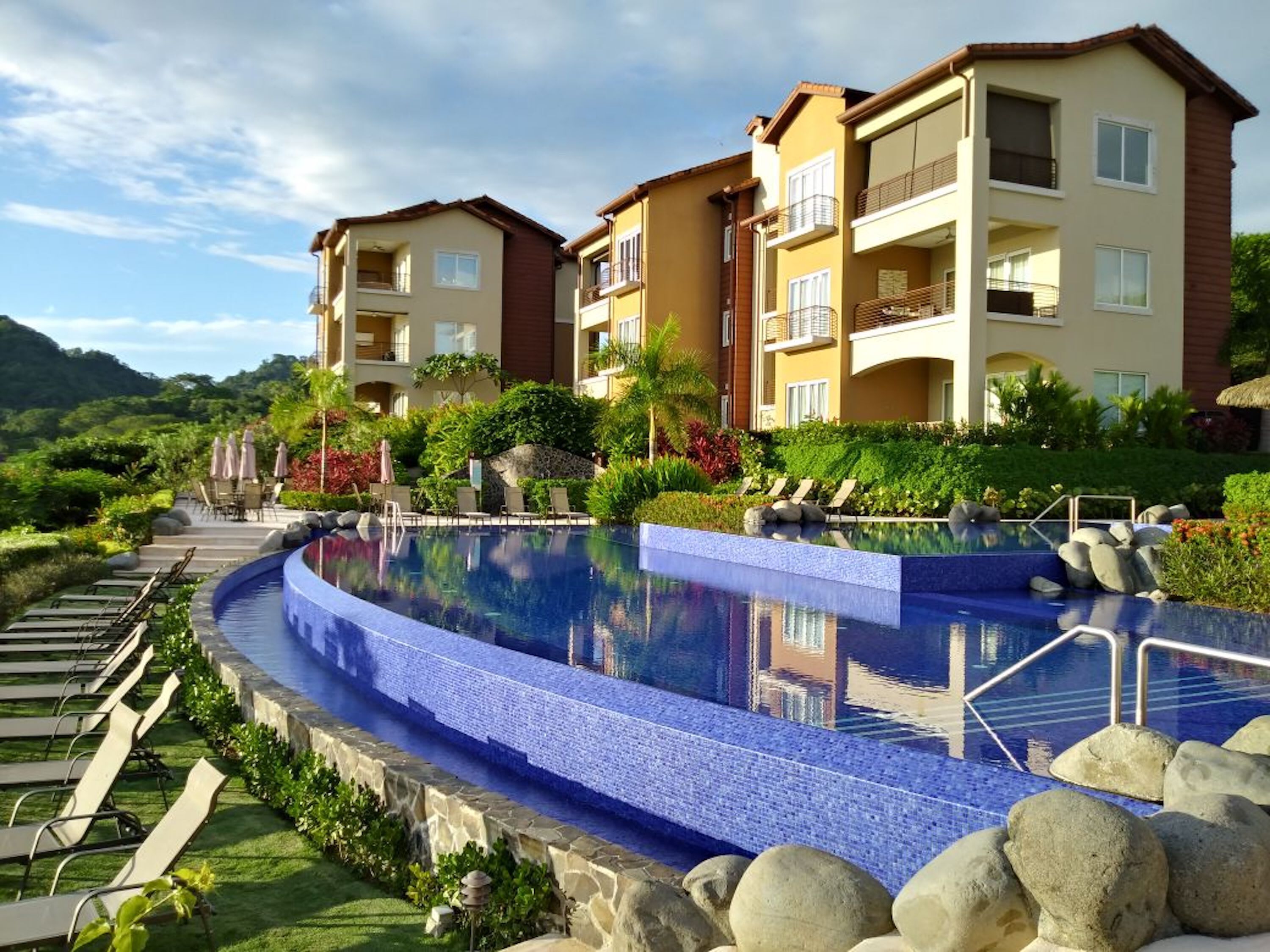 Un resort con piscina, sillas de descanso y montañas al fondo.