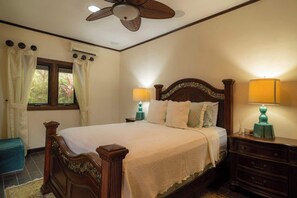 A bedroom with a wooden bed, two bedside lamps, a ceiling fan, and a window with curtains. - Casa Plazoleta 4 bdr private pool (Playa Herradura)
