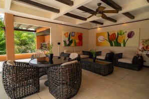 A spacious living area with a ceiling fan, outdoor view, and artwork on the walls. - Casa Plazoleta 4 bdr private pool (Playa Herradura)