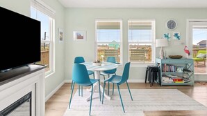 A modern living room with a flat-screen TV, a dining area with blue chairs, and a bookshelf. - Hot Tub, Pet Friendly, 4Bdr 2Bth, - Aqua Vista (Bolivar Peninsula)