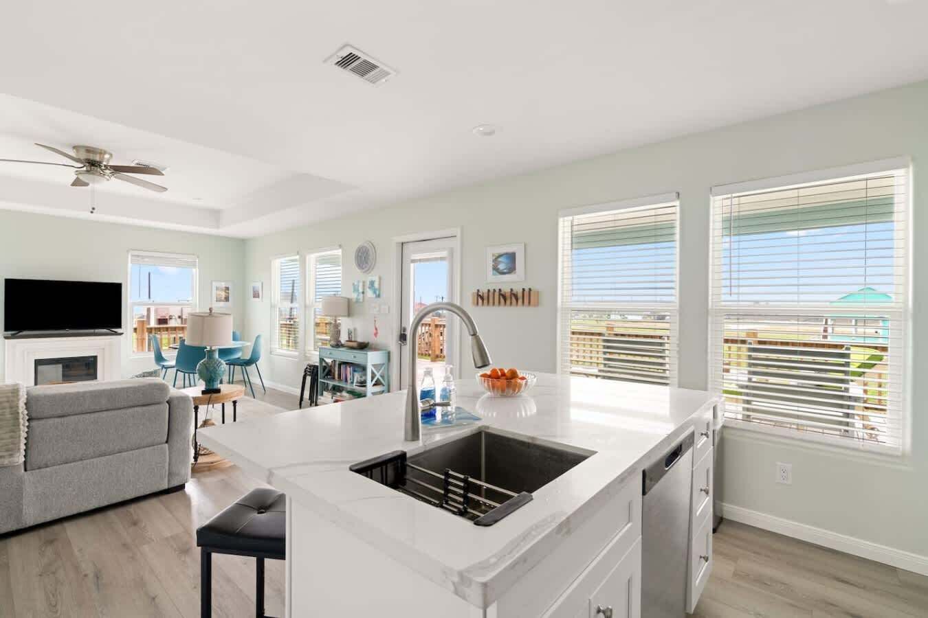 Una cucina moderna con isola centrale, un'area pranzo con sedie blu e un soggiorno con divano grigio.