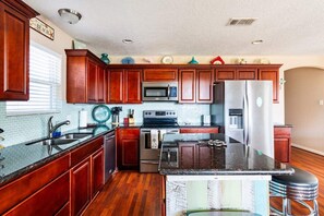 A kitchen with wooden cabinets, a stainless steel refrigerator, a microwave, and a stove. - Gulf Views, Pet Friendly, Deck (Bolivar Peninsula)