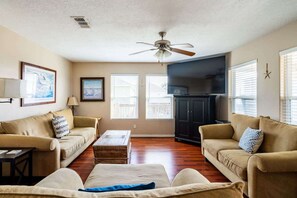 Ein Wohnzimmer mit zwei Sofas, einem Couchtisch, einem Deckenventilator und einem Fernseher.