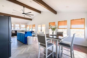 A modern kitchen with a blue island, a dining area with a table and chairs, and large windows with blinds.