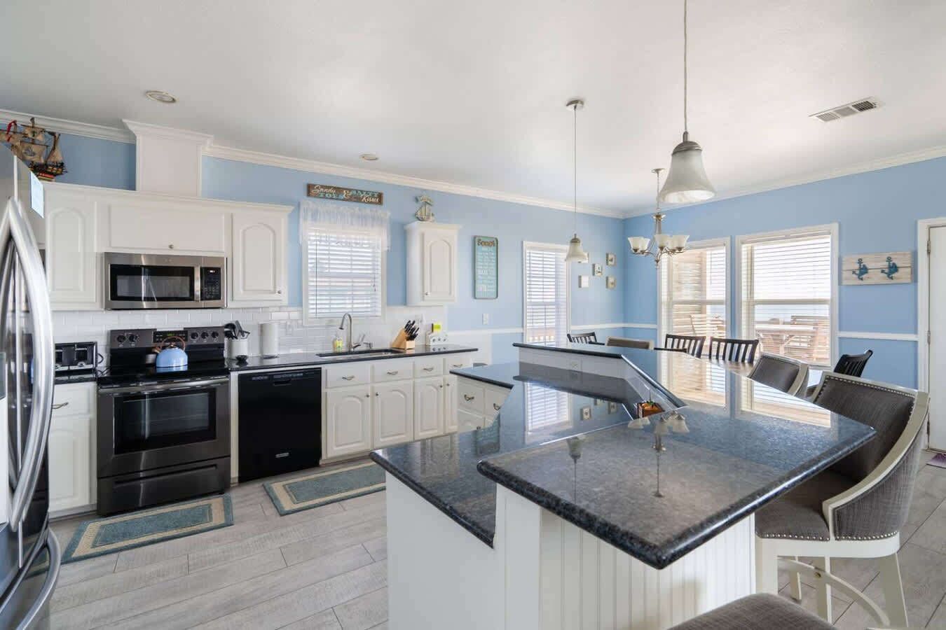 A modern kitchen with white cabinets, a central island, stainless steel appliances, and pendant lighting.