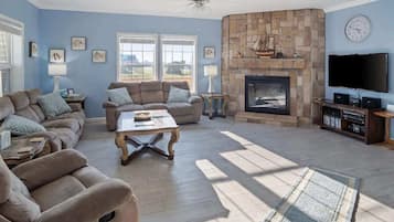 A living room with a stone fireplace, a flat-screen TV, and a large window.