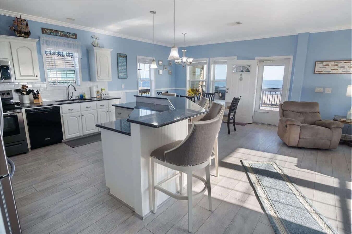 A modern kitchen with white cabinets, a central island, and a dining area with a chair.