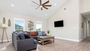 A living room with a sectional sofa, a coffee table, a ceiling fan, and a mounted TV. - Two Adjacent Cabins, Sleeps 18 (Bolivar Peninsula)