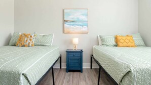 A room with two beds, each with patterned bedding, a nightstand with a lamp, and a framed picture on the wall. - Two Adjacent Cabins, Sleeps 18 (Bolivar Peninsula)