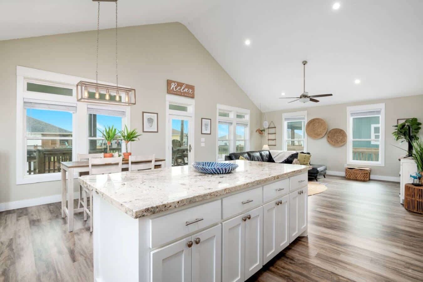 A spacious kitchen with a large island, white cabinetry, and a ceiling fan.