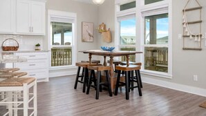 A spacious kitchen with white cabinetry, a wooden dining table, and large windows offering a view. - Two Adjacent Cabins, Sleeps 18 (Bolivar Peninsula)