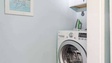 Un cuarto de lavandería con una lavadora, un estante con objetos y dos cuadros en la pared.