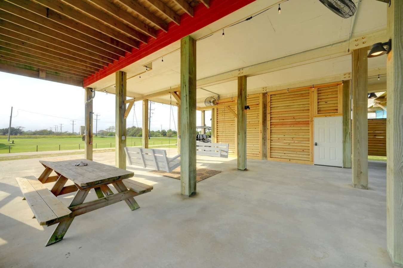 Un espacio al aire libre techado con mesas de picnic, una estructura de madera y vista a un campo verde.