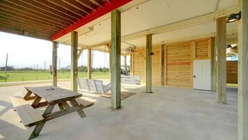 Un espacio al aire libre techado con mesas de picnic, una estructura de madera y vista a un campo verde.