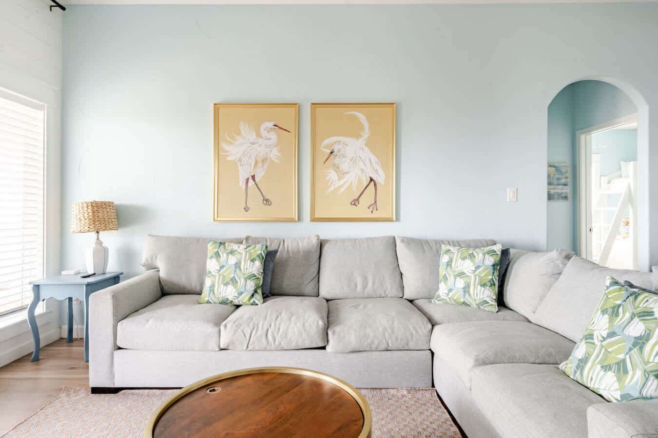 A living room with a light-colored sofa, two framed wall art pieces, a small side table with a lamp, and a round coffee table.