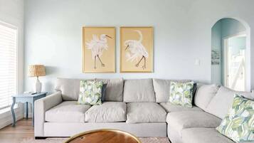 A living room with a light-colored sofa, two framed wall art pieces, a small side table with a lamp, and a round coffee table.