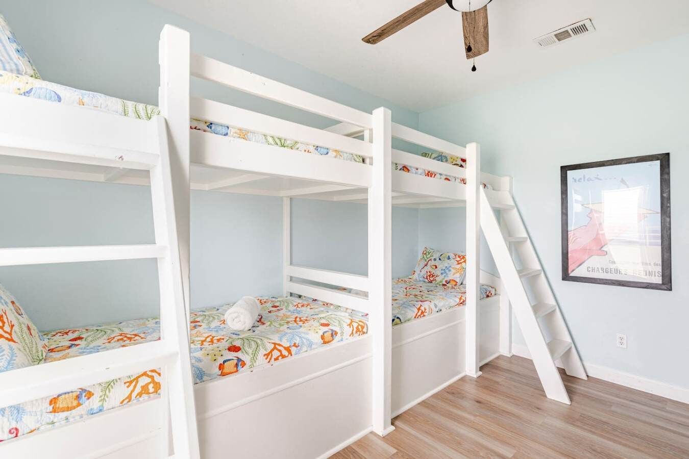 Habitación con literas, una escalera, un cartel en la pared y un ventilador de techo.