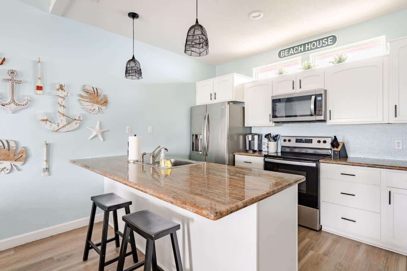 A modern kitchen with white cabinets, a granite island, black bar stools, and pendant lights.
