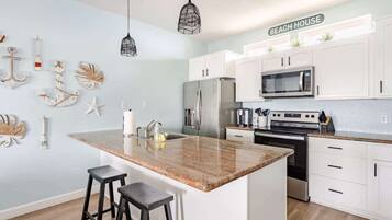 A modern kitchen with white cabinets, a granite island, black bar stools, and pendant lights.