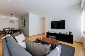 A modern living room with a sofa, coffee table, flat-screen TV, and a dining area with a table and chairs. - Capitalia  Business Center, Gym & Parking (Ciudad de México)