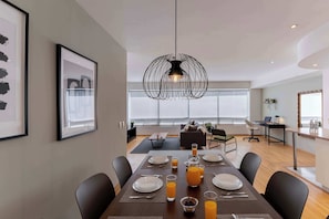 A modern dining area with a large table set for breakfast, a unique black pendant light, and a city view through large windows. - Capitalia  Business Center, Gym & Parking (Ciudad de México)