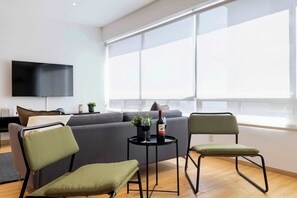 A modern living room with a sofa, two chairs, a small table with a bottle and glasses, and a TV mounted on the wall. - Capitalia  Business Center, Gym & Parking (Ciudad de México)