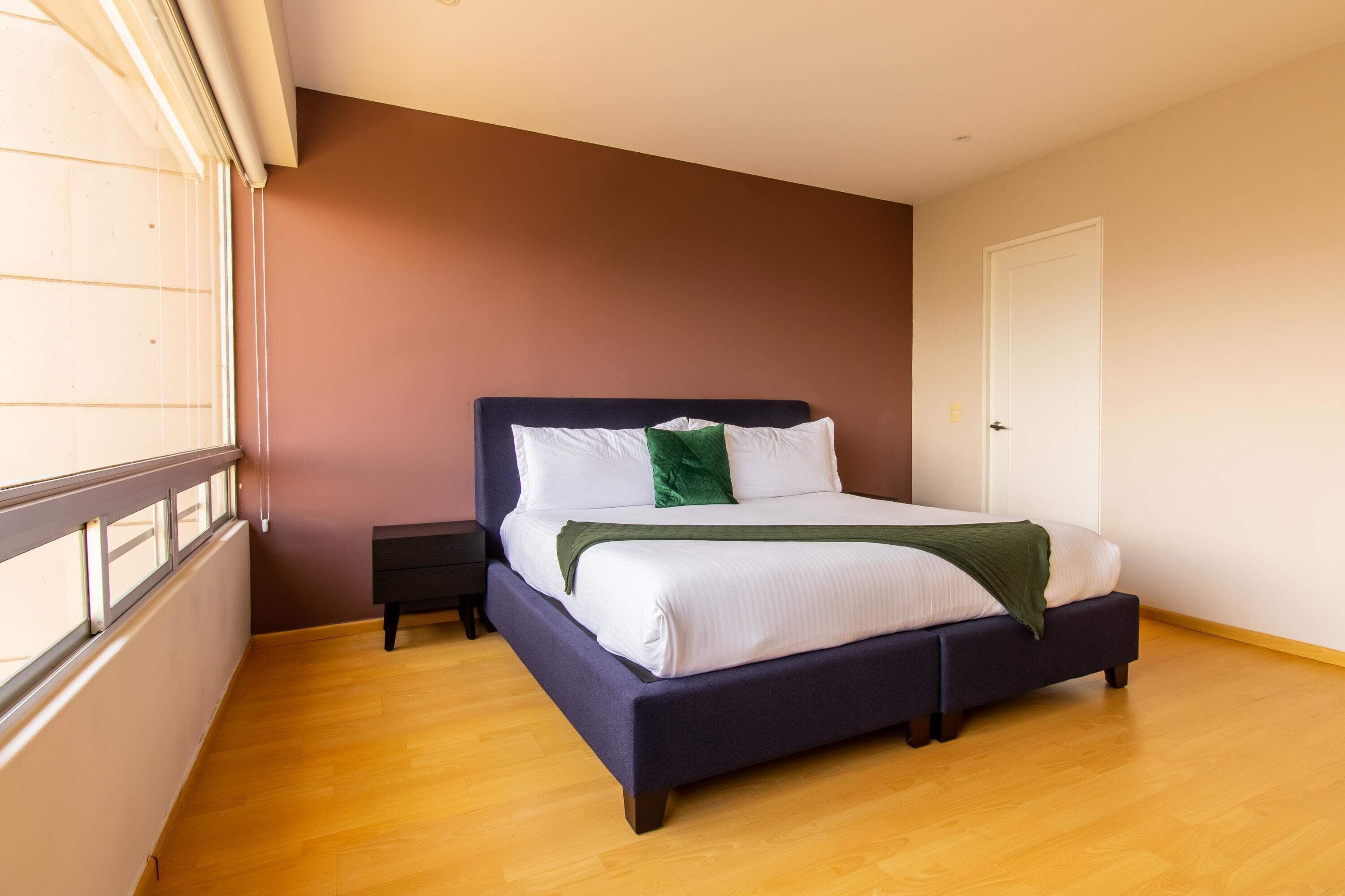 A bedroom with a bed, a nightstand, a window, and a door.