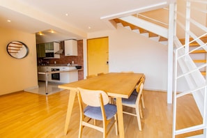 A modern kitchen with wooden cabinets, a dining table with chairs, and a staircase.