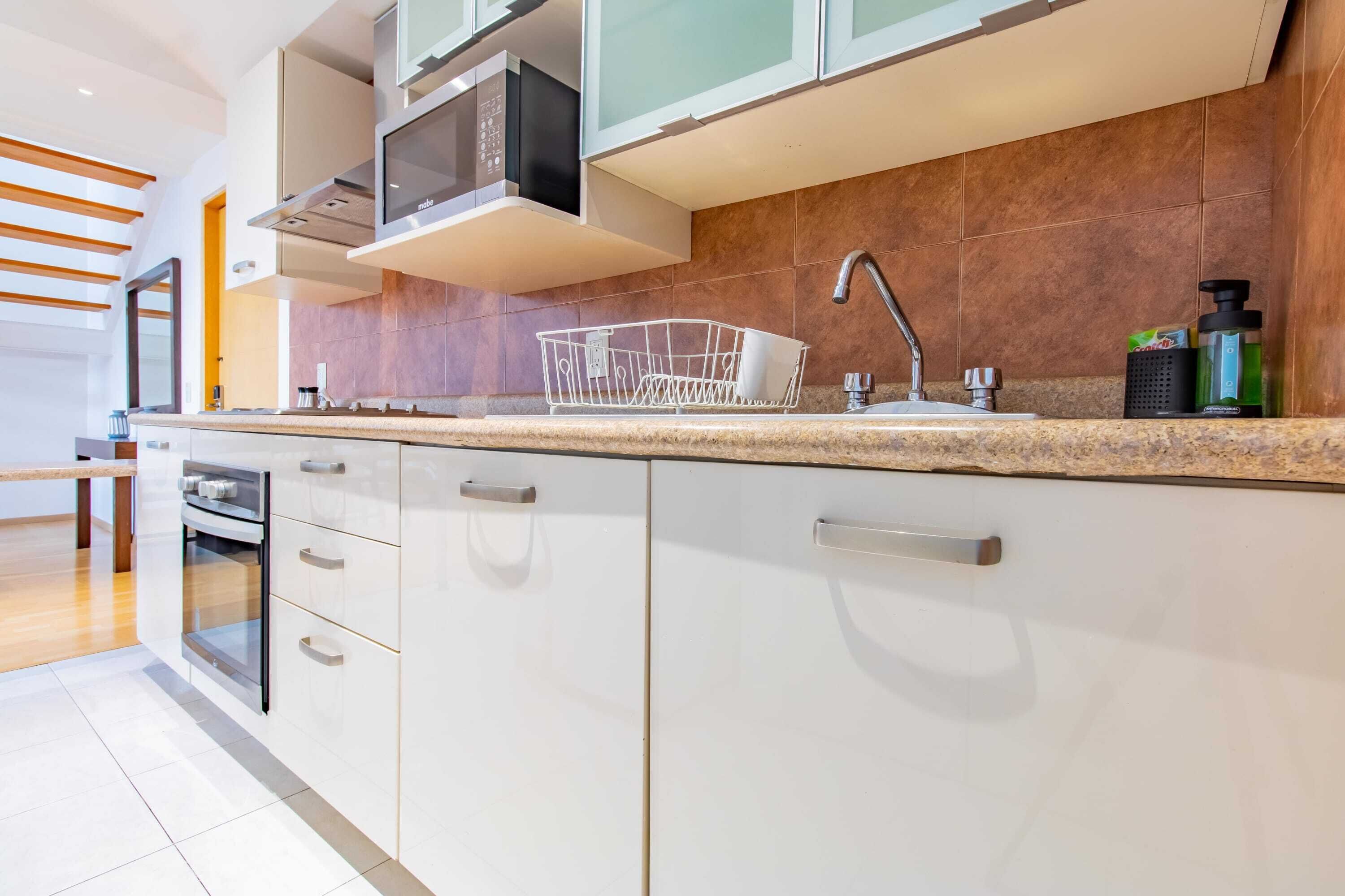 A modern kitchen with white cabinets, a stainless steel oven, a microwave, and a dish rack.