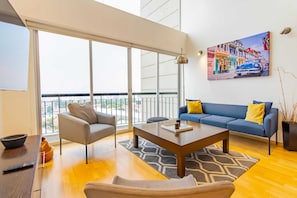 A modern living room with a sofa, armchair, coffee table, and a painting on the wall.