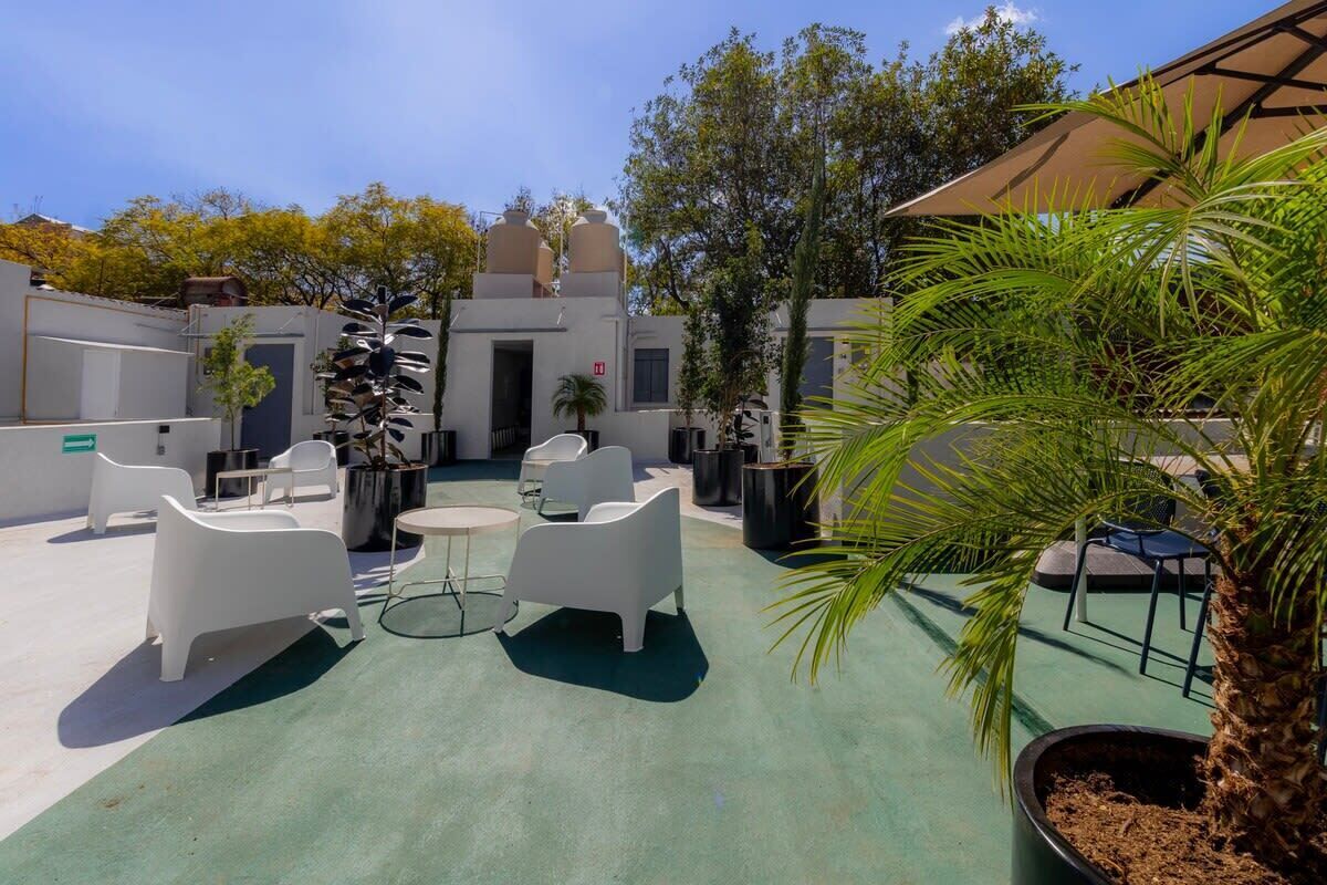 An outdoor patio area with white chairs and tables, surrounded by potted plants and trees.