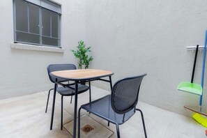 A small outdoor seating area with a round table and two chairs, a window, a potted plant, and cleaning tools. - Capitalia , Nuevo Polanco, Patio & Pet Friendly (Ciudad de México)
