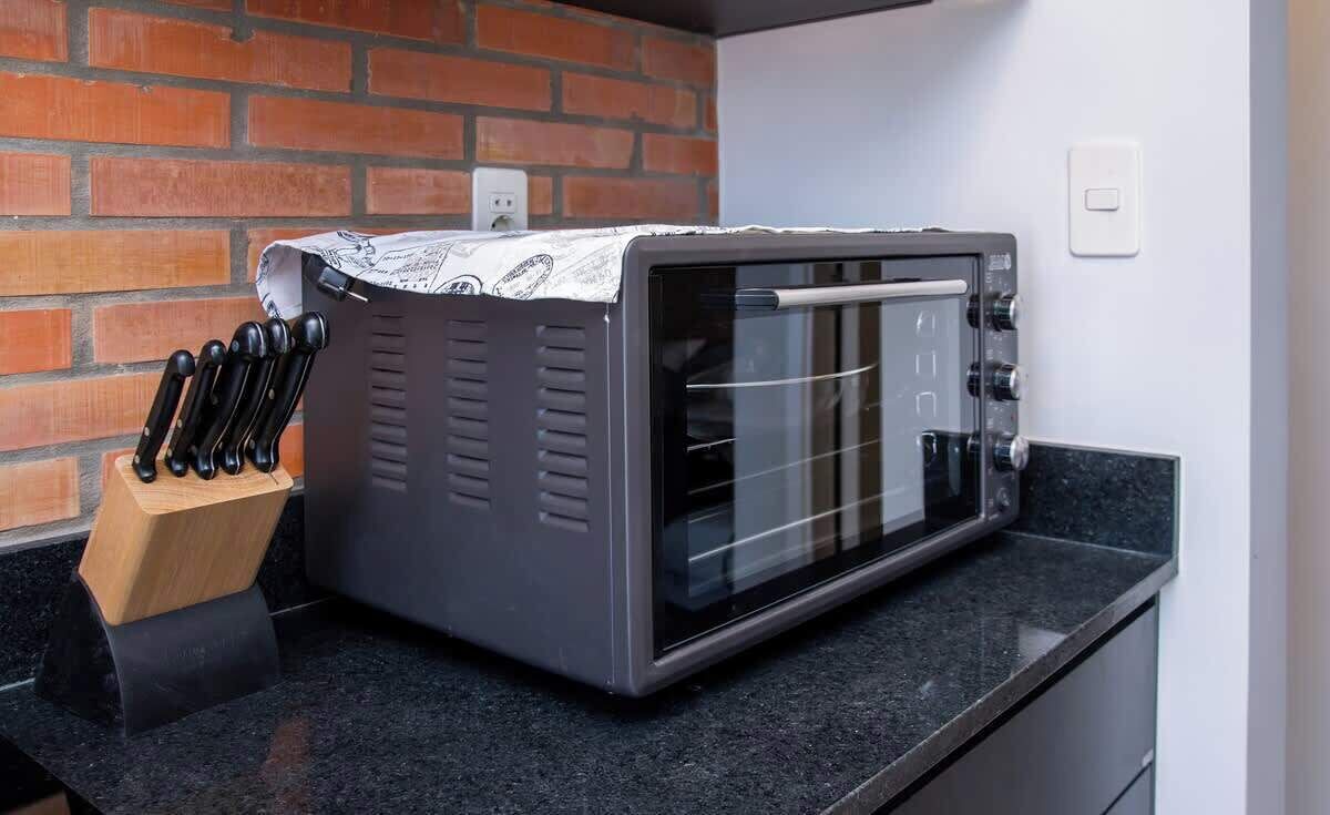 A kitchen with a microwave oven, a knife block, and a brick wall.