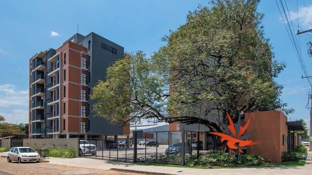 A multi-story building with balconies, a parking area, and a distinctive red sculpture. - Modern 2BR Apt with Balcony Free Parking B53 (Asunción)
