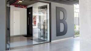 A modern building entrance with a glass door, a large letter 'B' on the wall, and a visible fire extinguisher. - Modern 2BR Apt with Balcony Free Parking B53 (Asunción)